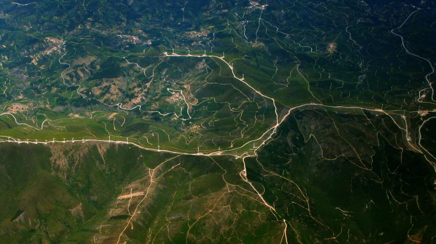 Wind turbines and access roads across a mountainous green landscape