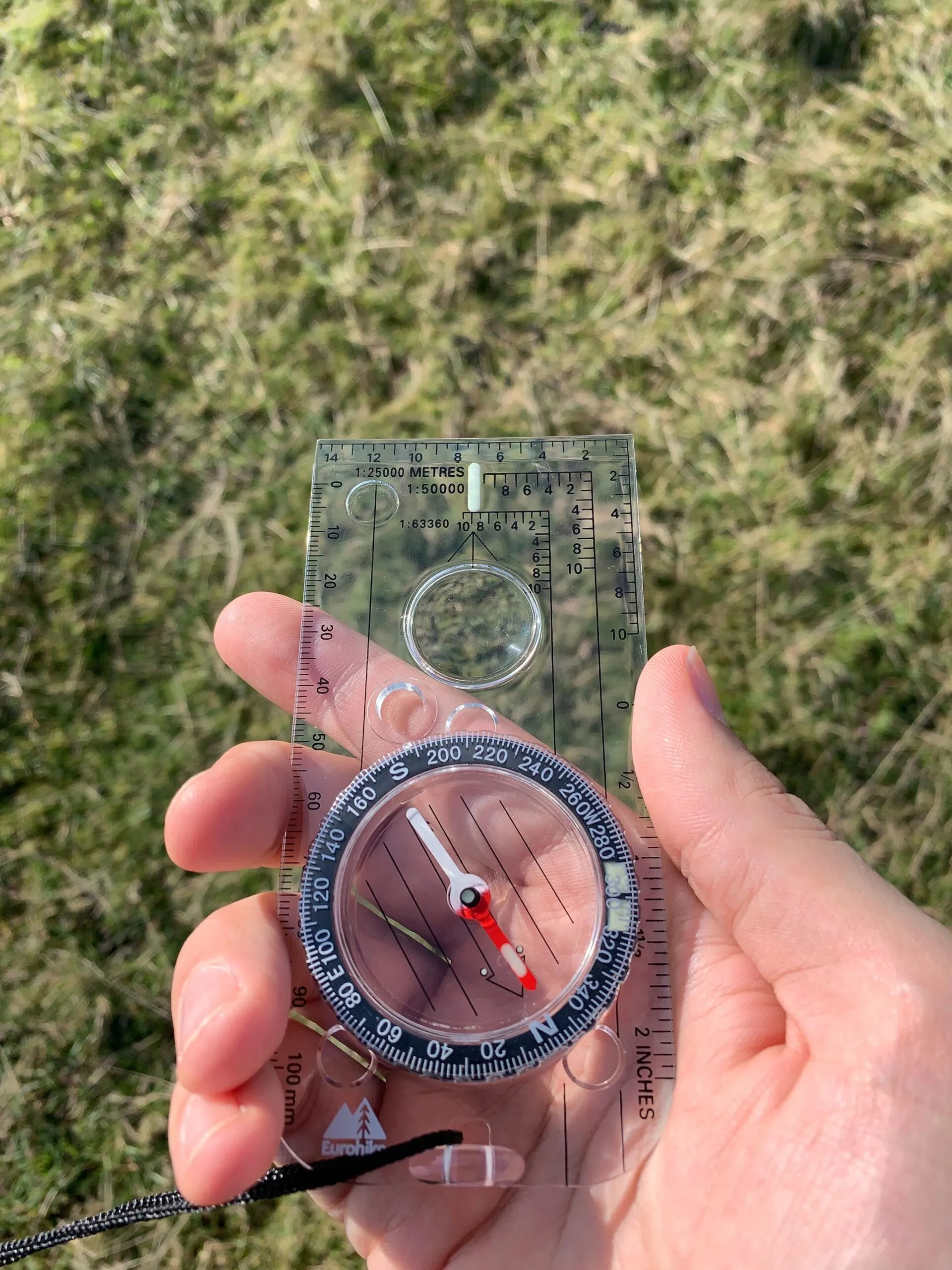 A hand holding a compass over grass