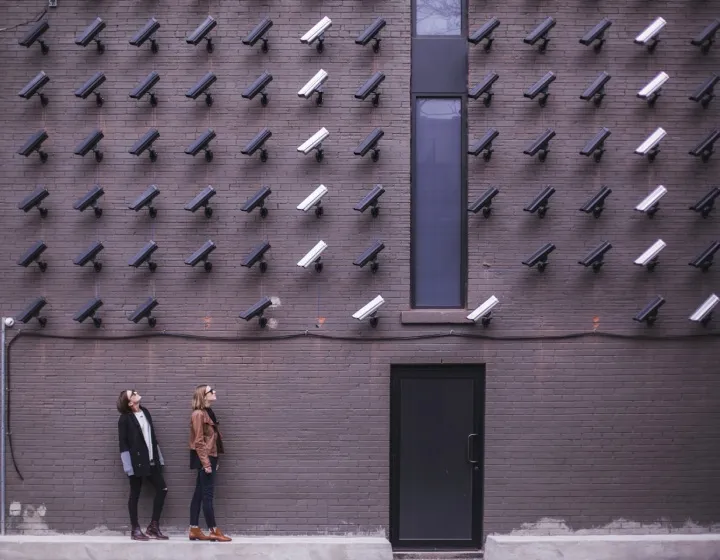 Two people looking at a wall covered with security cameras