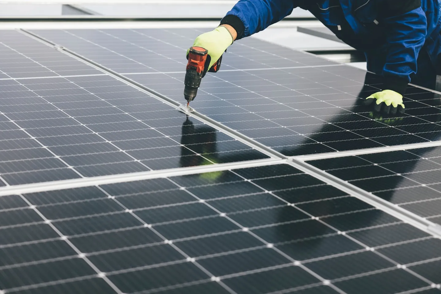 A worker installing solar panels with a power drill