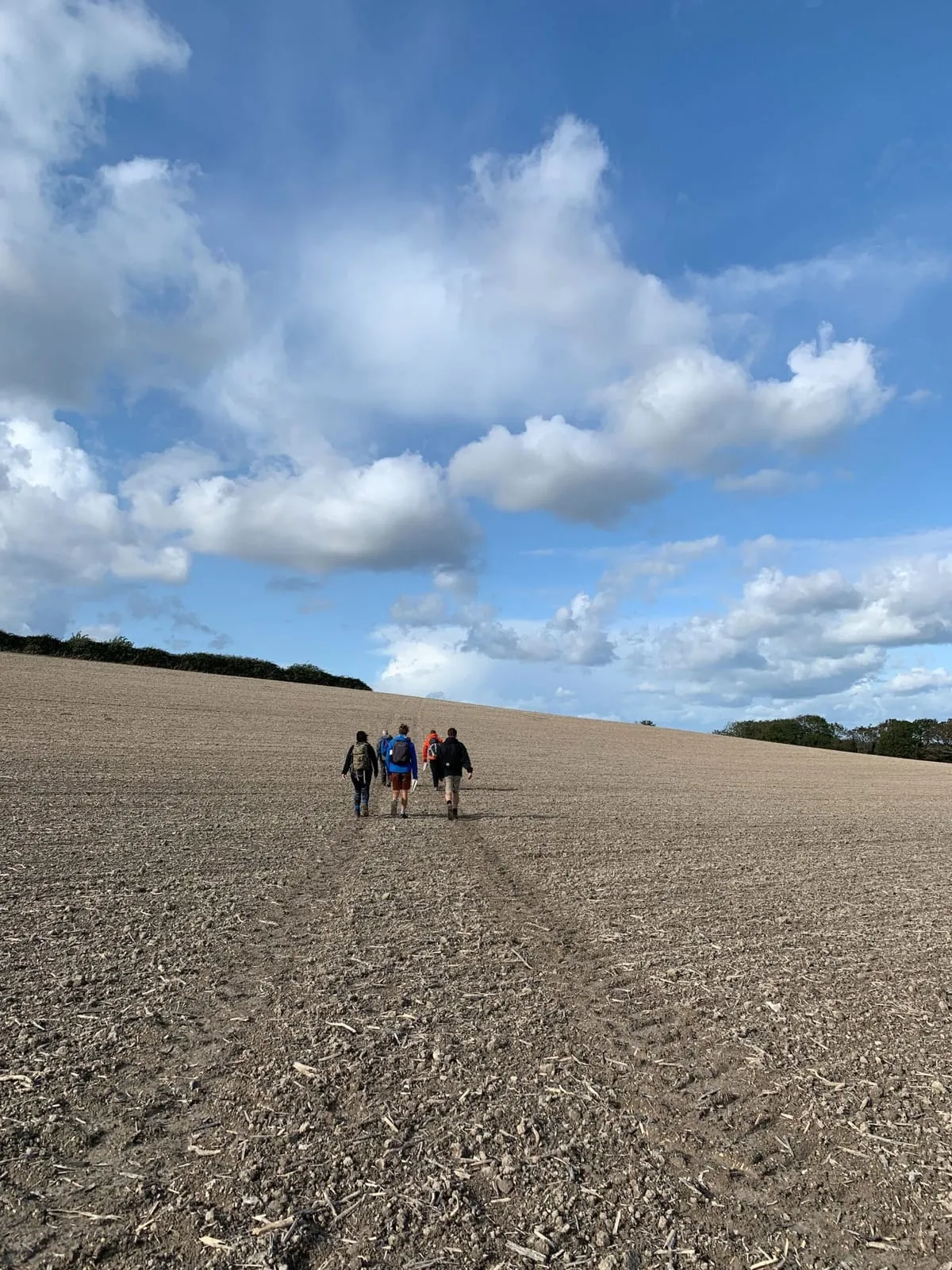 Team members walking across a ploughed field beneath a wide blue sky